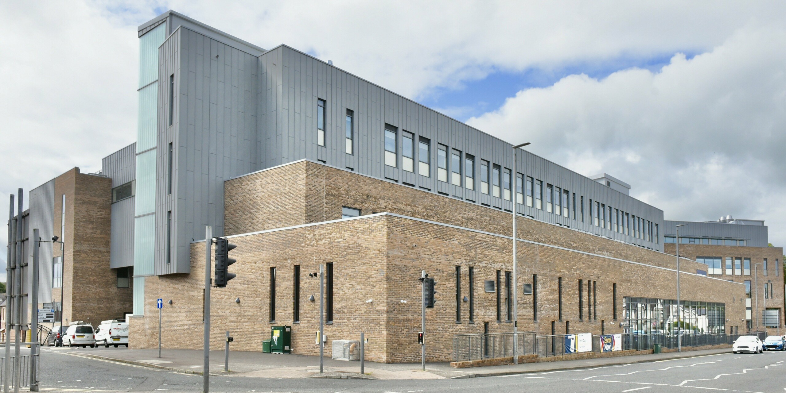 Blick auf den Zufahrtsbereich des North Regional College in Coleraine. Die PREFALZ Aluminiumfassade in Patinagrau setzt einen modernen Kontrast zur historischen Backsteinarchitektur und bietet durch die Stehfalzverkleidung dauerhafte Beständigkeit und gestalterische Eleganz.