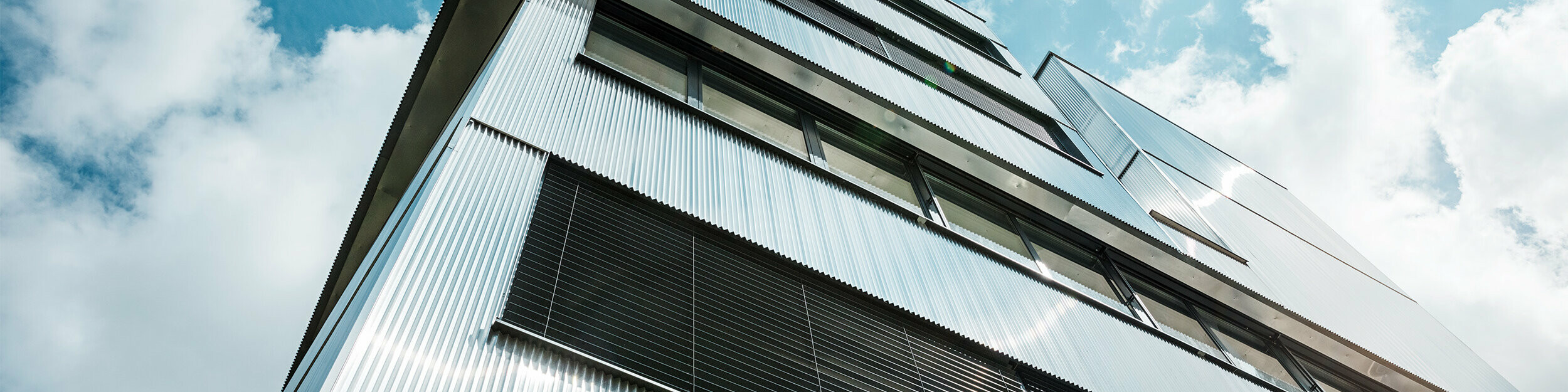 Nahaufnahme der PREFA Fassade einer Musikschule in Bjevolar mit Zackenprofil. Die Fassade besteht aus einer Kombination von schwarzen und aluminiumblanken Aluminiumoberflächen, die in der Sonne glänzen und das moderne Design unterstreichen.