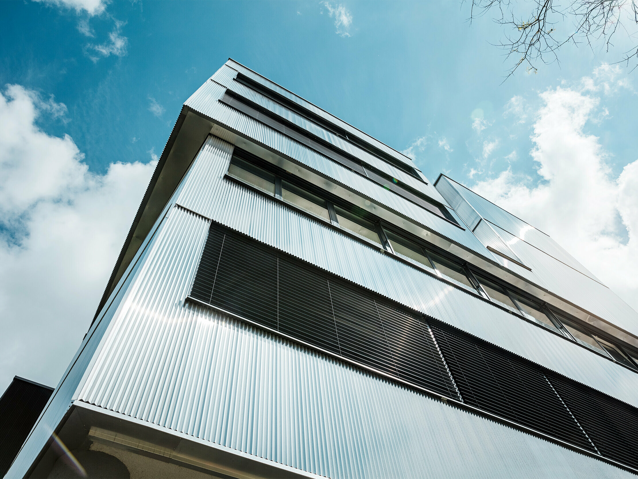 Nahaufnahme der PREFA Fassade einer Musikschule in Bjevolar mit Zackenprofil. Die Fassade besteht aus einer Kombination von schwarzen und aluminiumblanken Aluminiumoberflächen, die in der Sonne glänzen und das moderne Design unterstreichen.