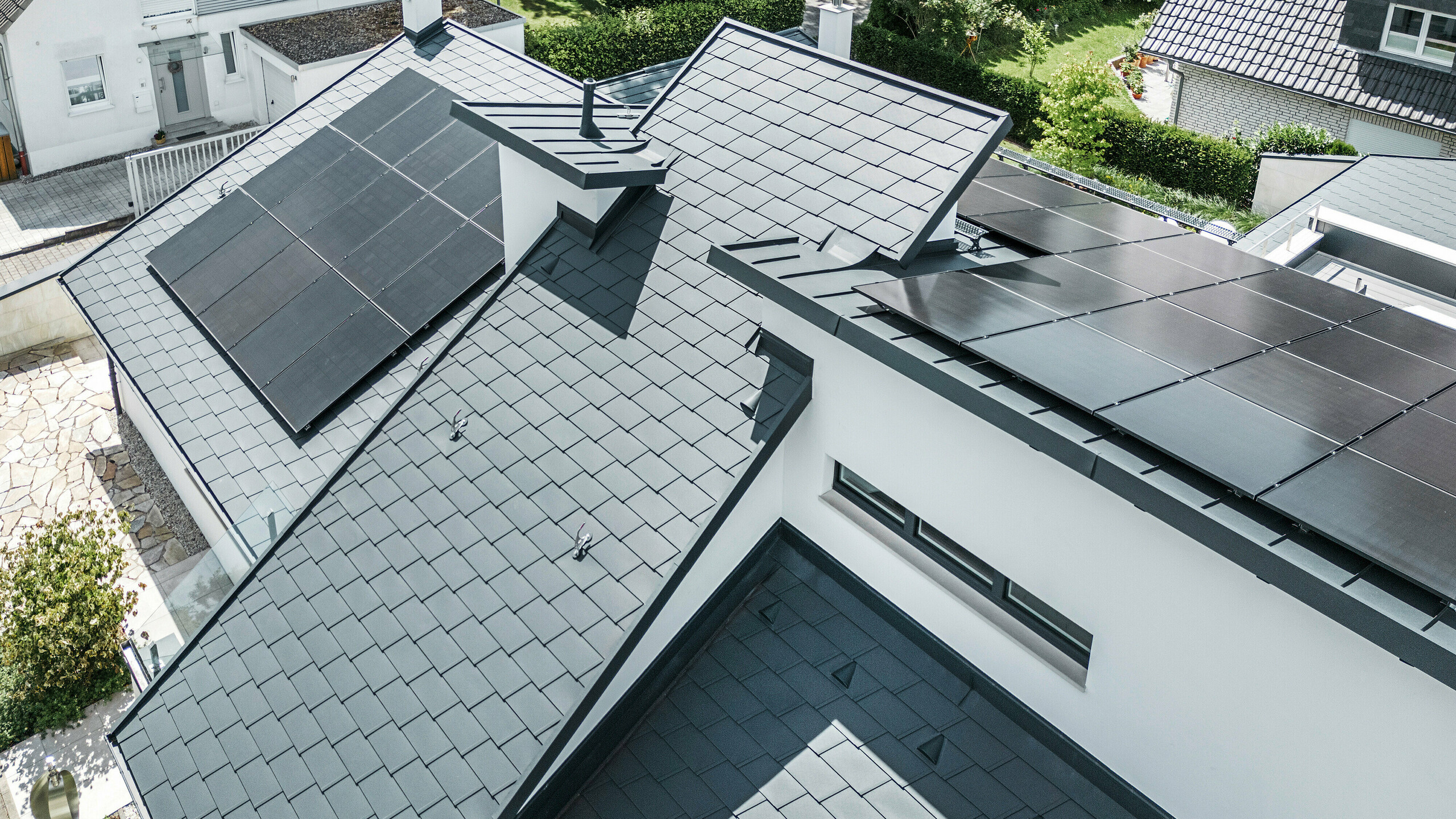 Pogled iz ptičje perspektive na različite razine na krovu moderne obiteljske kuće u Dortmundu opremljen je PREFA krovnom šindrom DS.19 i PREFALZ u boji P.10 antracit kao i velikim PV sustavom.