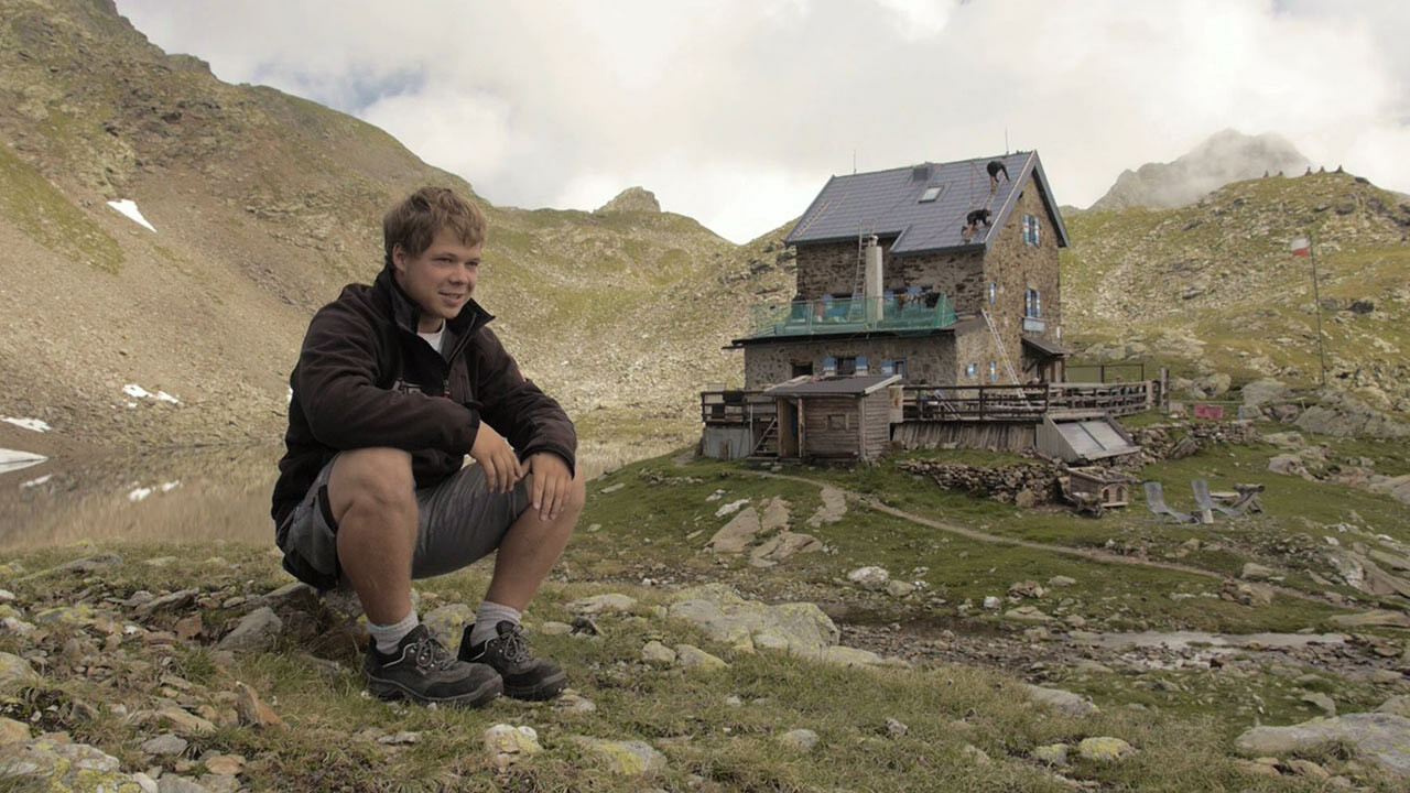 Naučnik Jakob Schöttl sjedi na kamenu. U pozadini se može vidjeti planinska koliba „Flagger Schartenhütte” koja je ponovno pokrivena PREFA krovnom pločom.